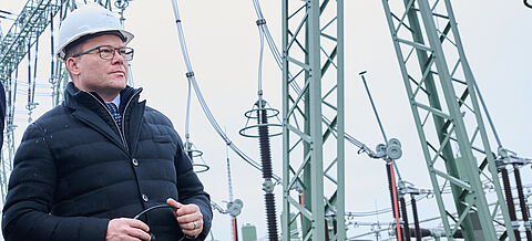 Bundesumweltminister Schneider mit Helm steht vor Strommasten