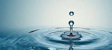 Ein Tropfen Wasser trifft auf eine Wasserfläche und erzeugt dabei kleine Wellen