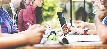 Jugendliche sitzen in einer Gruppe am Tisch und arbeiten an Laptops