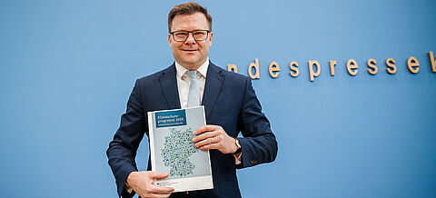 Carsten Schneider hält das Klimaschutzprogramm 2026 in die Kamera.